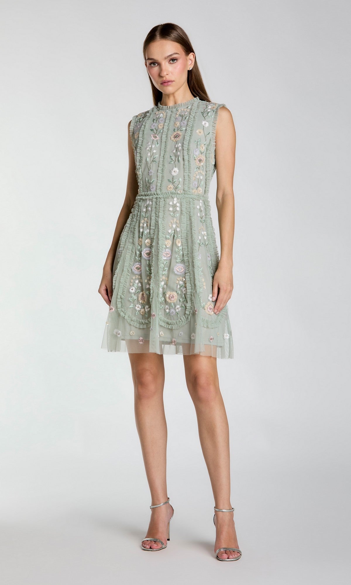 A woman wears the Mac Duggal 9135 Embroidered Short Party Dress in light green, featuring floral details, posed against a plain background and styled with strappy high-heeled sandals.